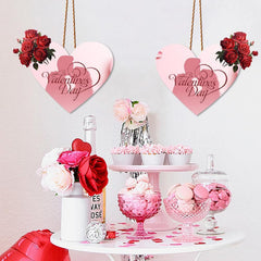 Valentine's Day-themed decor with heart-shaped signs, flowers, and sweets on a table.