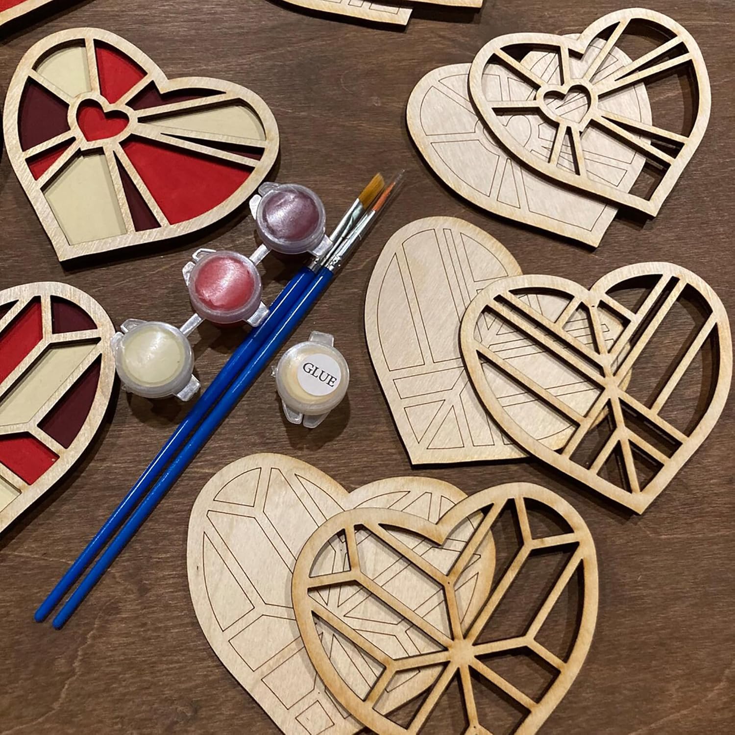 Wooden heart-shaped crafts with paint, brushes, and glue on a wooden surface