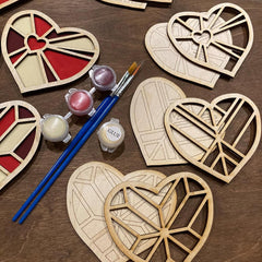 Wooden heart-shaped crafts with paint, brushes, and glue on a wooden surface