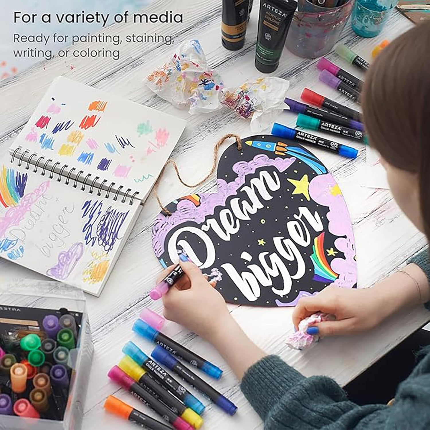 Person working on a craft project with markers and art supplies on a table.