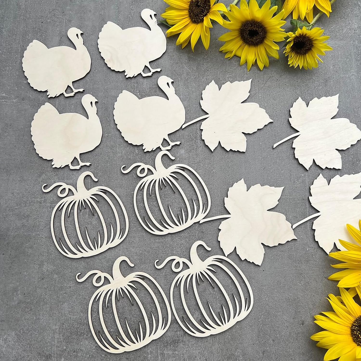 White paper cutouts of turkeys, pumpkins, and leaves on a gray background with sunflowers.