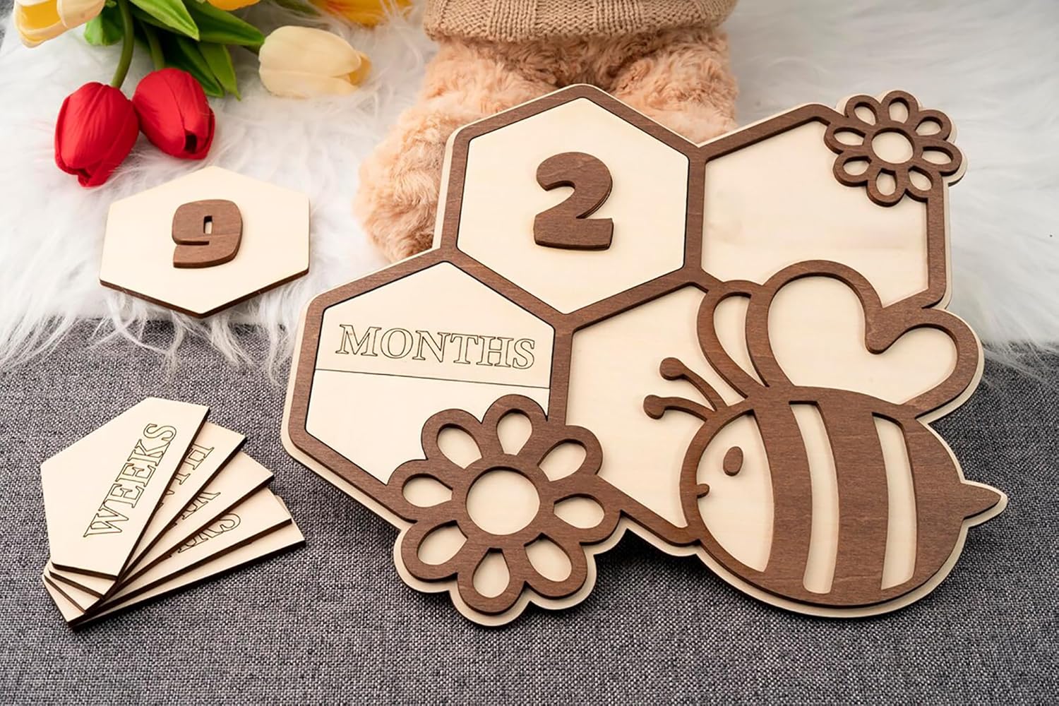 Wooden baby milestone card with bee and flower design, showing '2 months' and '9 weeks'.
