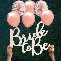 Rose gold balloons with 'Bride to be' sign against a dark background