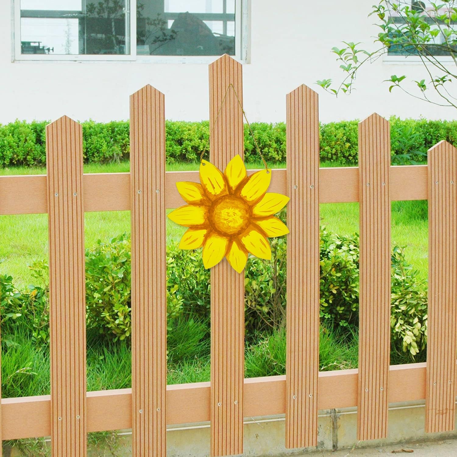 Wooden picket fence with a decorative sunflower in front of greenery