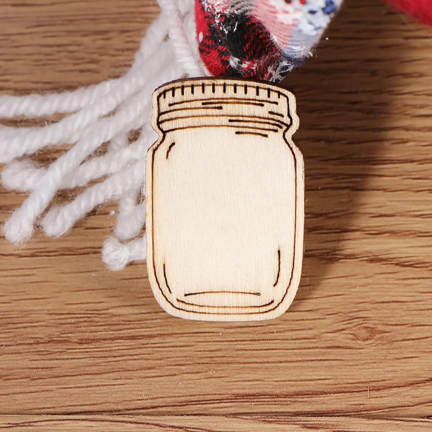 Wooden mason jar ornament on a wooden surface with white yarn in the background