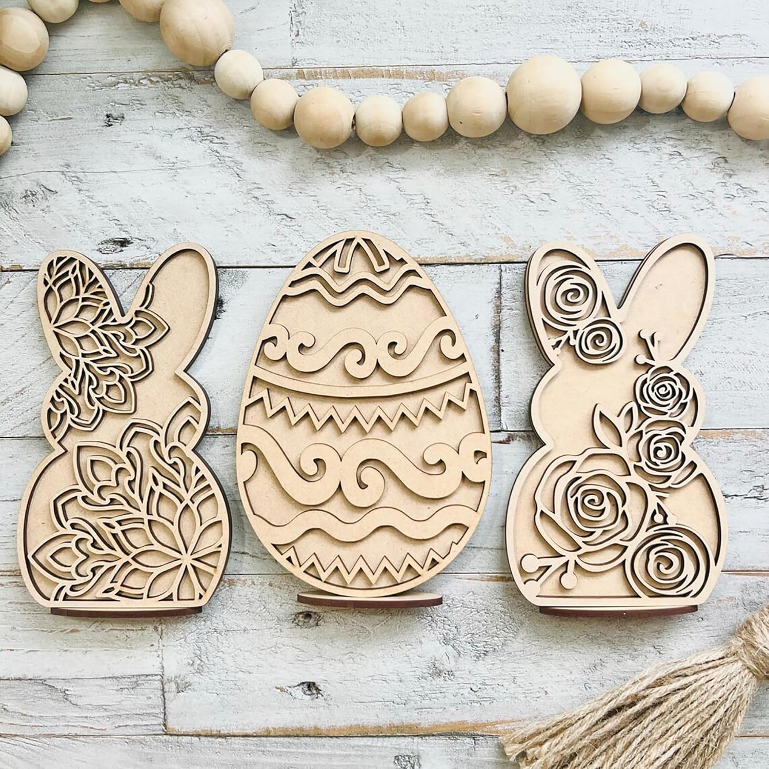 Three wooden Easter decorations shaped like rabbits and an egg on a rustic wooden surface.