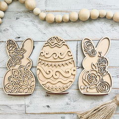 Three wooden Easter decorations shaped like rabbits and an egg on a rustic wooden surface.