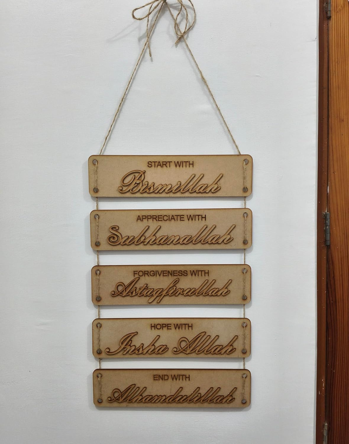 Wooden plaque with engraved Arabic phrases on a white wall.