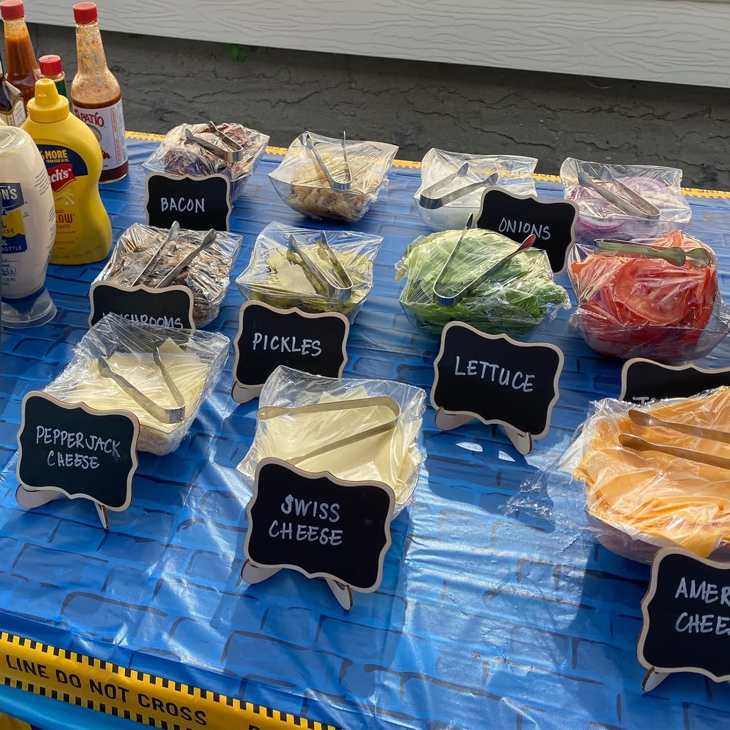 Assorted deli meats and cheeses on a blue tarp with labeled signs.