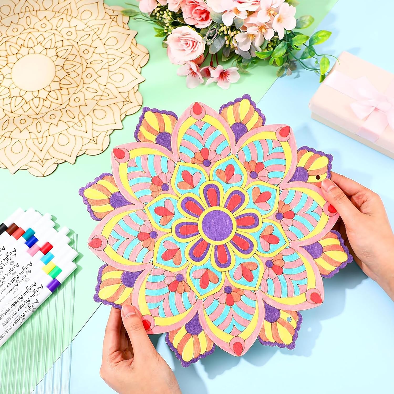 Colorful mandala art being held by a hand on a light blue surface with floral decorations.
