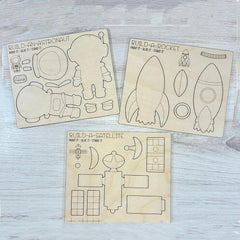 Wooden cutouts of astronaut, rocket, and satellite with assembly lines on a light wooden surface.