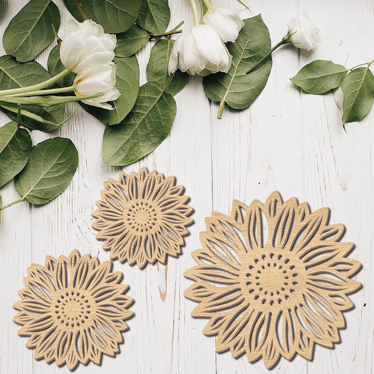 Three sunflower-shaped wooden coasters on a white wooden surface with green leaves and white flowers.