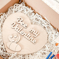 Heart-shaped wooden plaque with 'Bee my Valentine' text on a white crinkled paper background