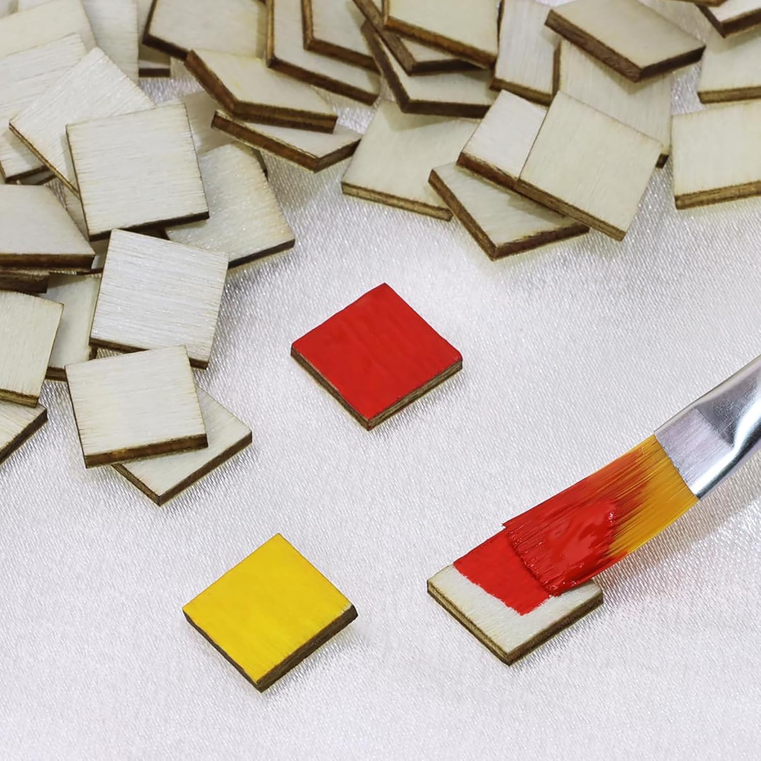 Small square tiles with paintbrush applying red paint on a white surface