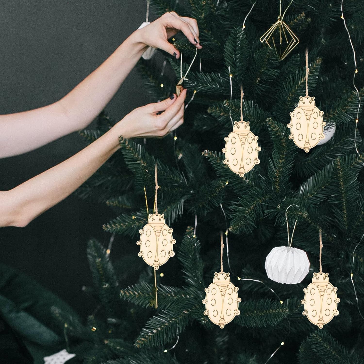 Person decorating a Christmas tree with gold and white ornaments against a dark background
