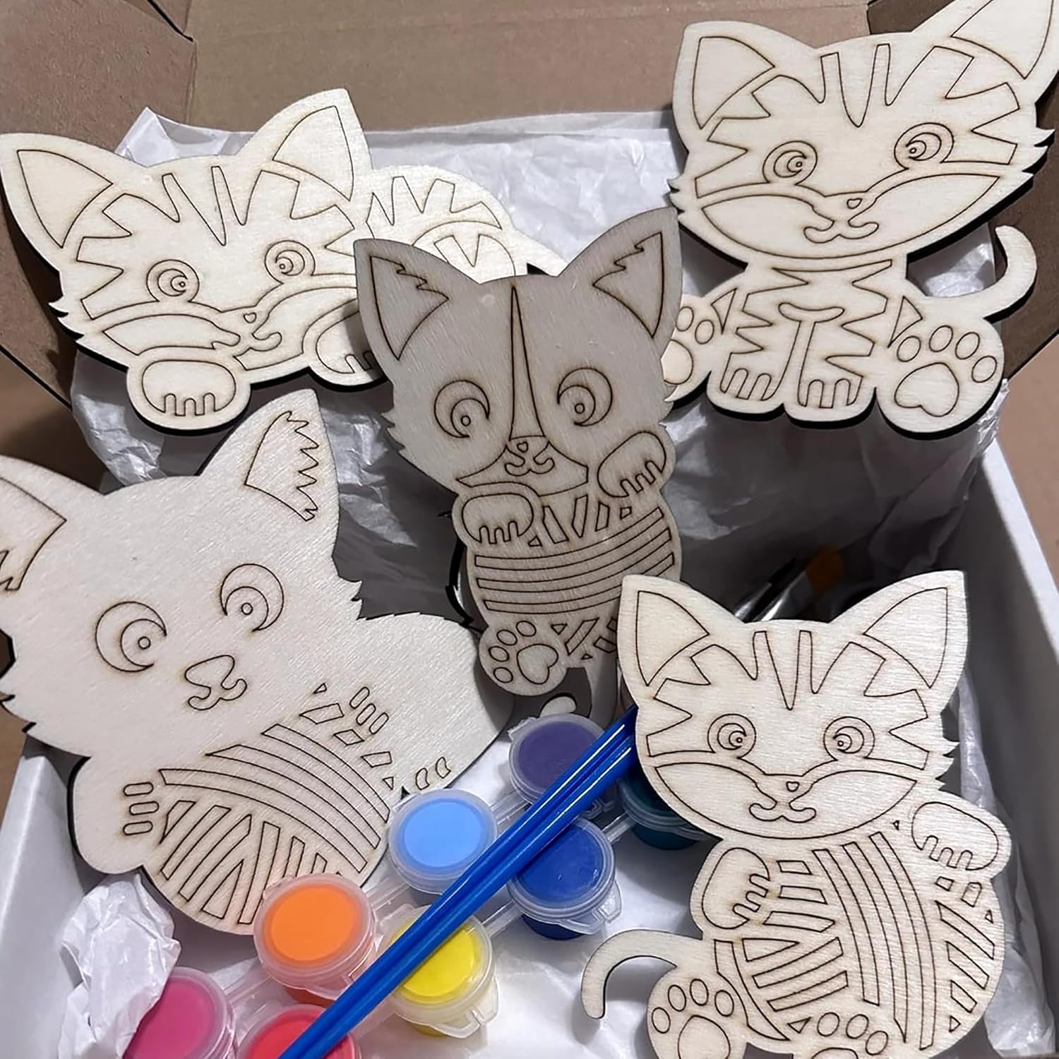 Wooden cat-shaped cutouts with paint supplies on a white surface