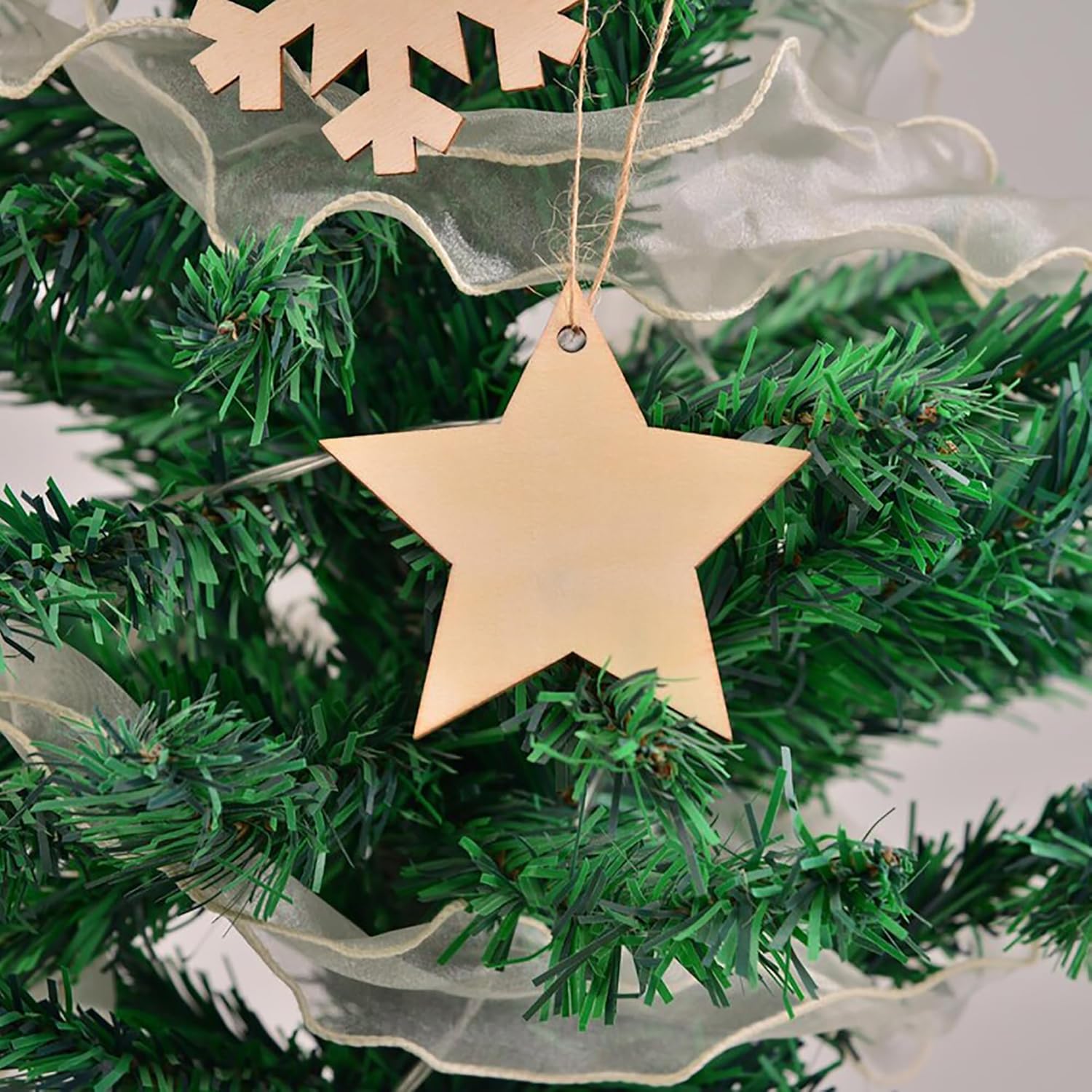 Gold star ornament hanging on a green Christmas tree with white tinsel