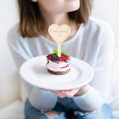 Person holding a small cake with a 'I am sorry' heart-shaped topper.