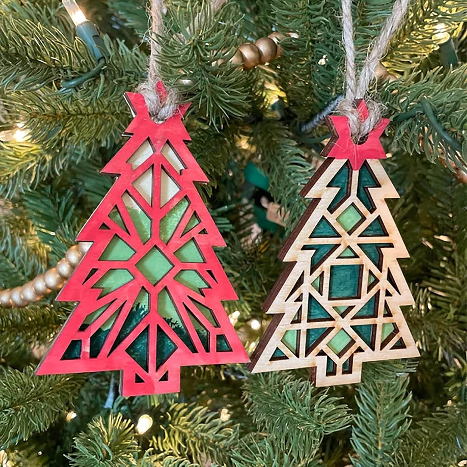 Two geometric Christmas tree ornaments hanging on a decorated tree.