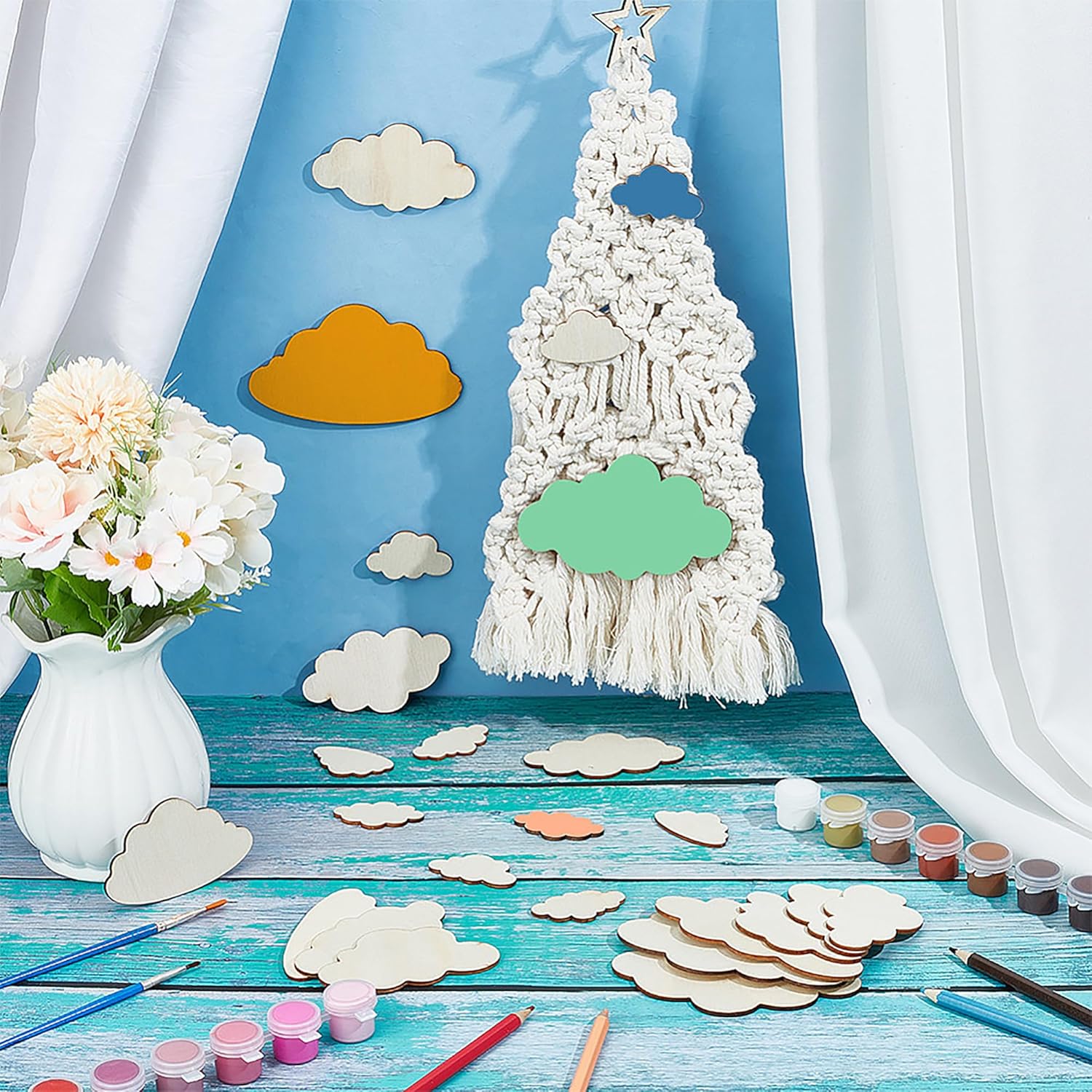 Crafting setup with a decorative tree made of yarn and cutout clouds on a blue background.
