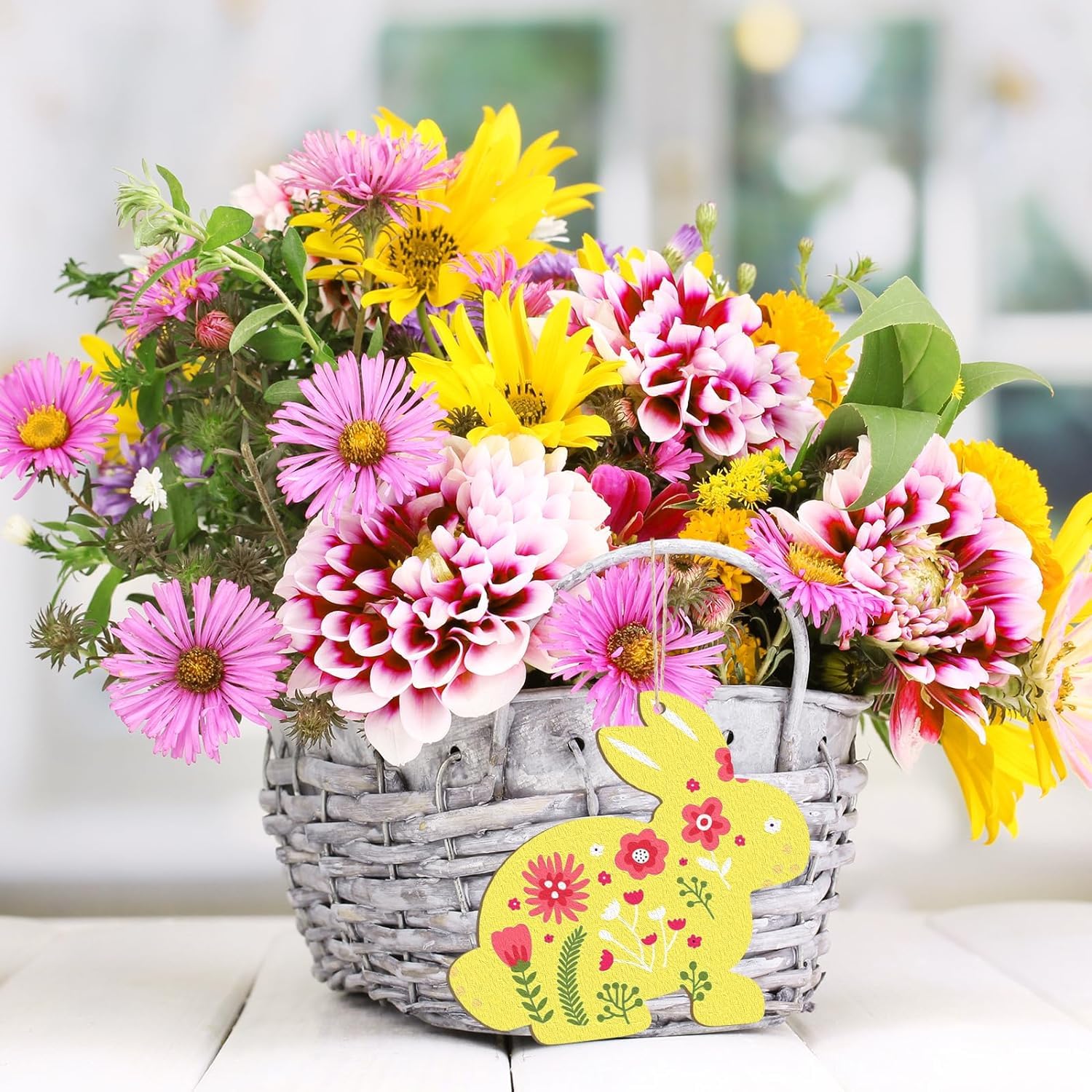 Bouquet of colorful flowers in a basket with a decorative bunny tag on a blurred background
