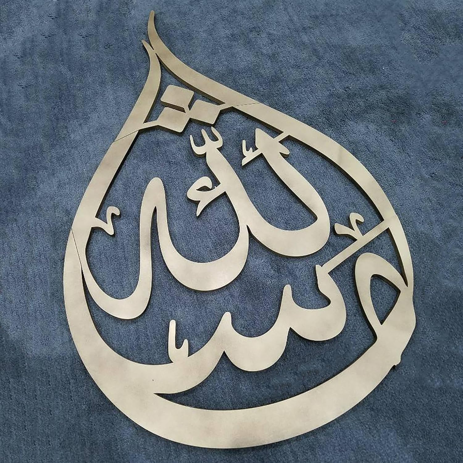 Decorative metal art piece with Arabic calligraphy on a blue fabric background