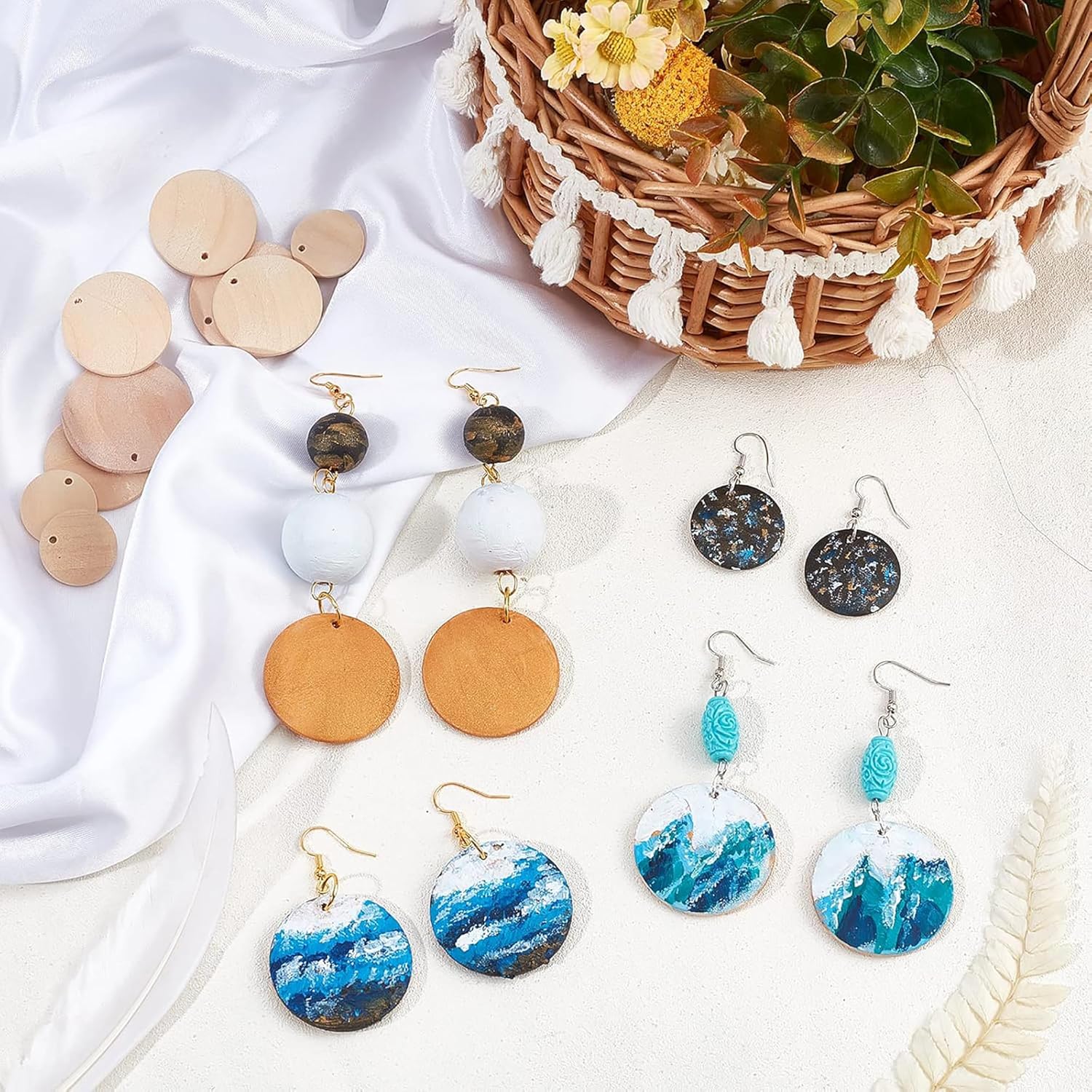 Collection of earrings on a white surface with a woven basket and flowers in the background.