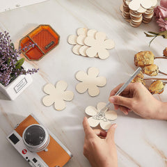 Person decorating wooden flower shapes with a small tool on a table with a camera and flowers.