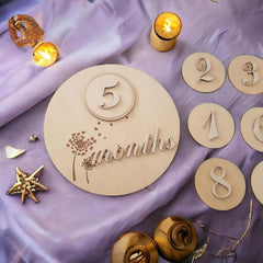 Wooden milestone plaque with '5 months' on a purple fabric background with decorative items.