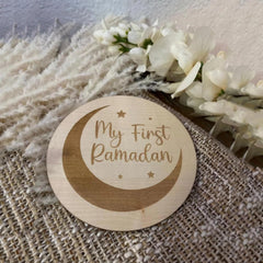 Wooden disc with 'My First Ramadan' engraving on a textured surface with flowers.