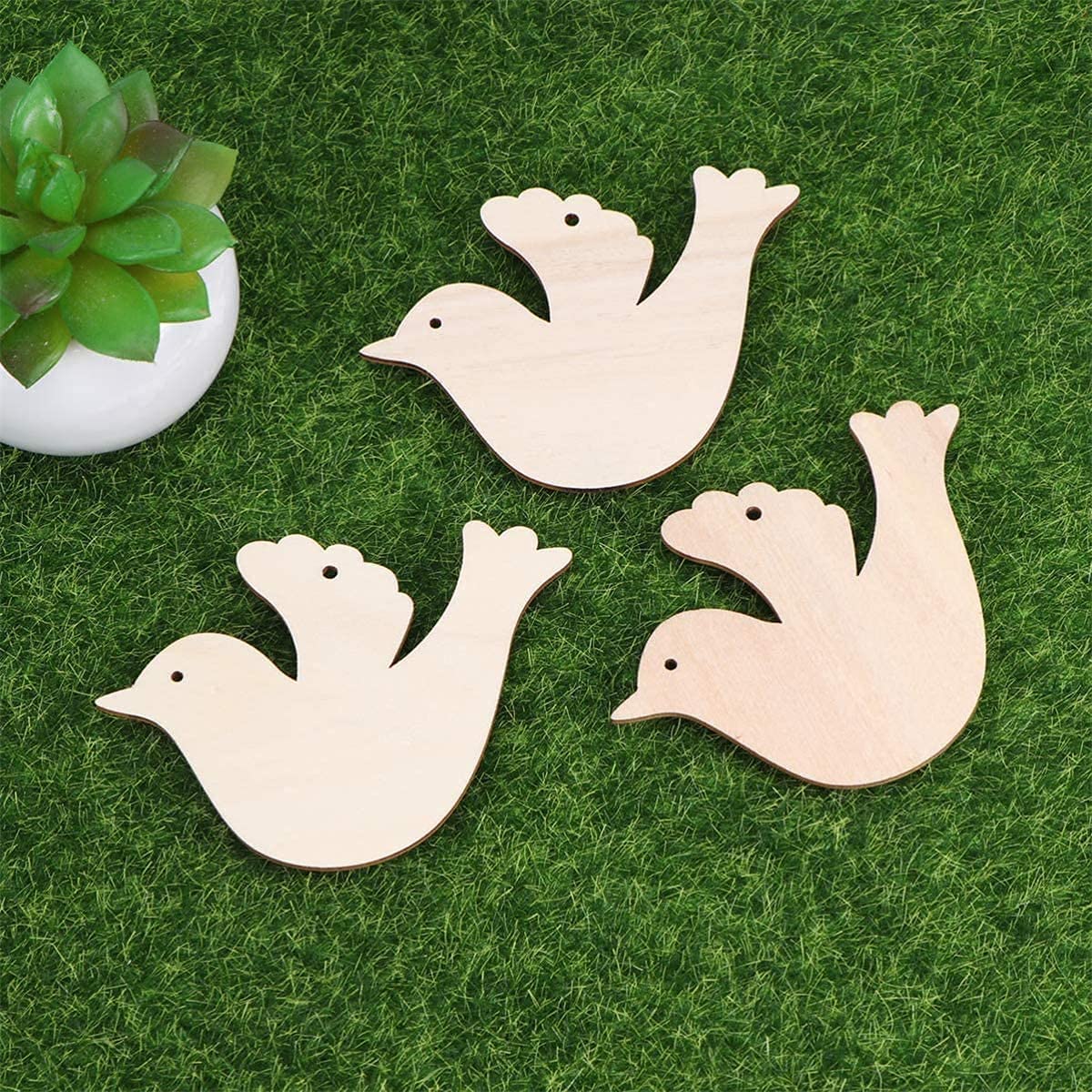 Three wooden dove shapes on a grassy surface with a small plant in the corner.