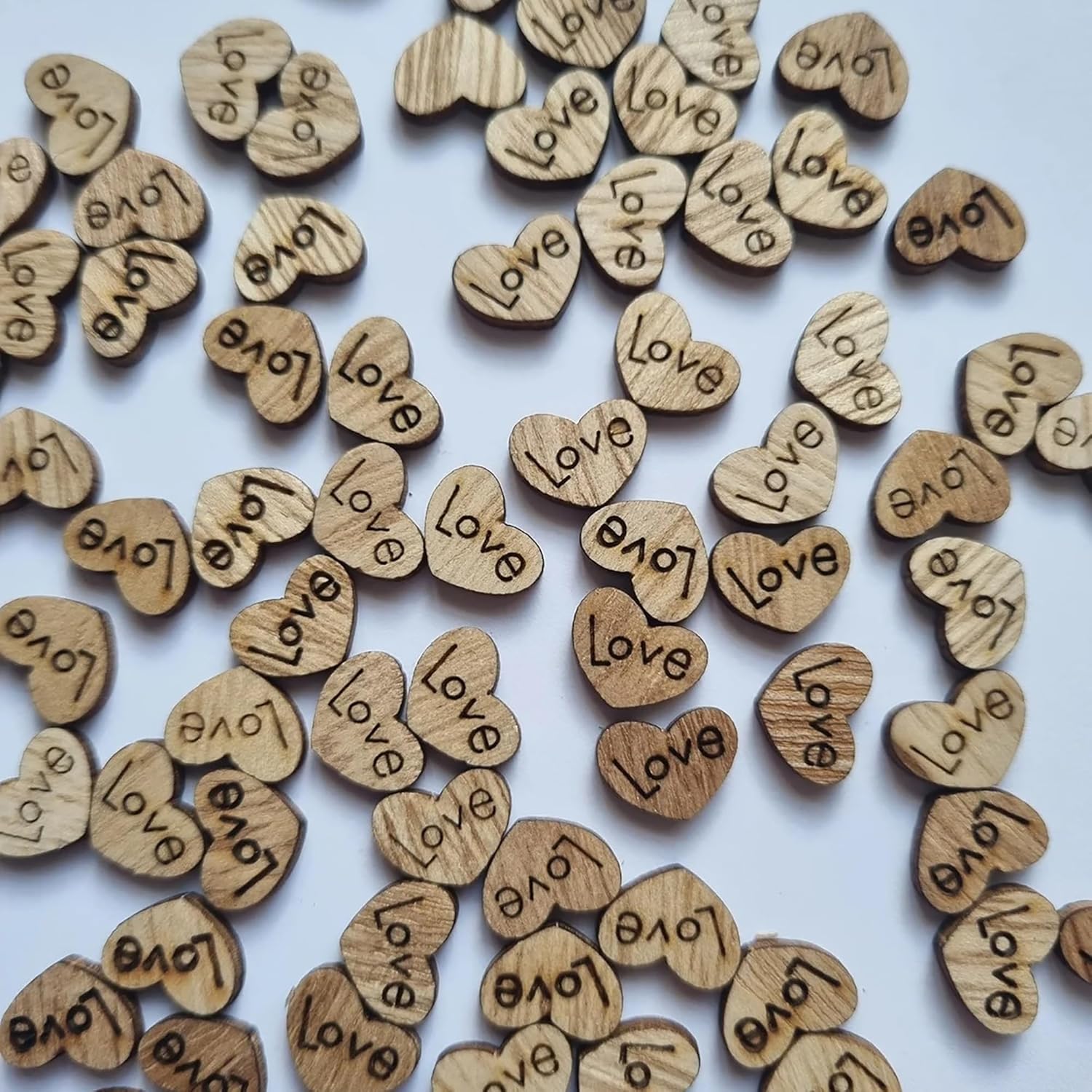 Wooden hearts with 'Love' engraved on them scattered on a white background