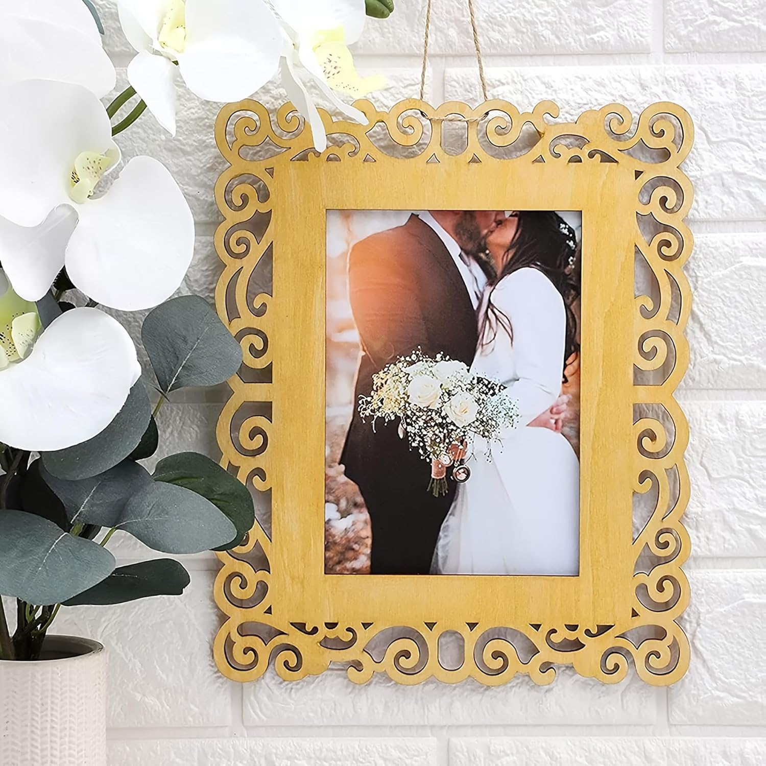 Decorative yellow frame with a wedding photo of a couple holding flowers, placed on a textured white surface with flowers in the background.
