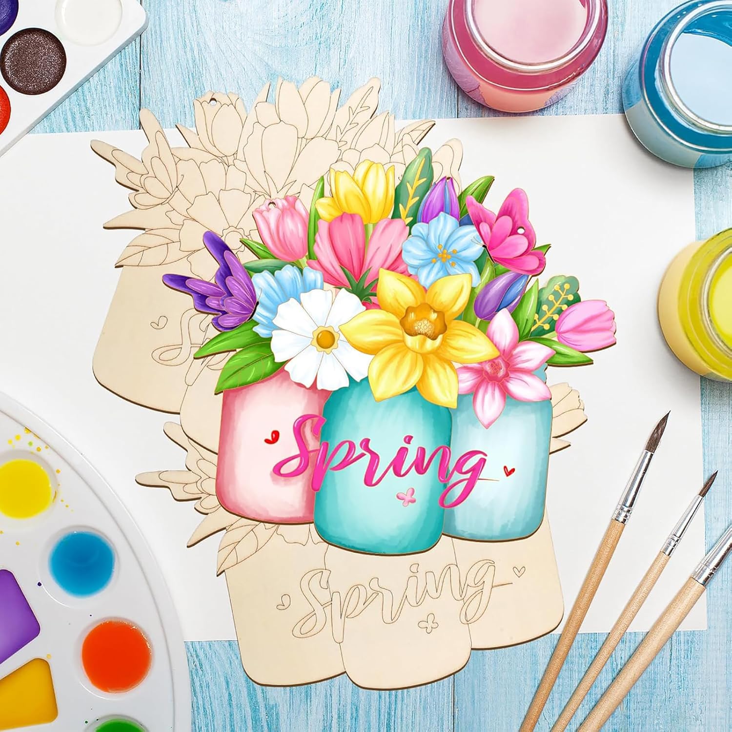 Colorful spring-themed painting with flowers and 'Spring' text on a wooden board, surrounded by art supplies.