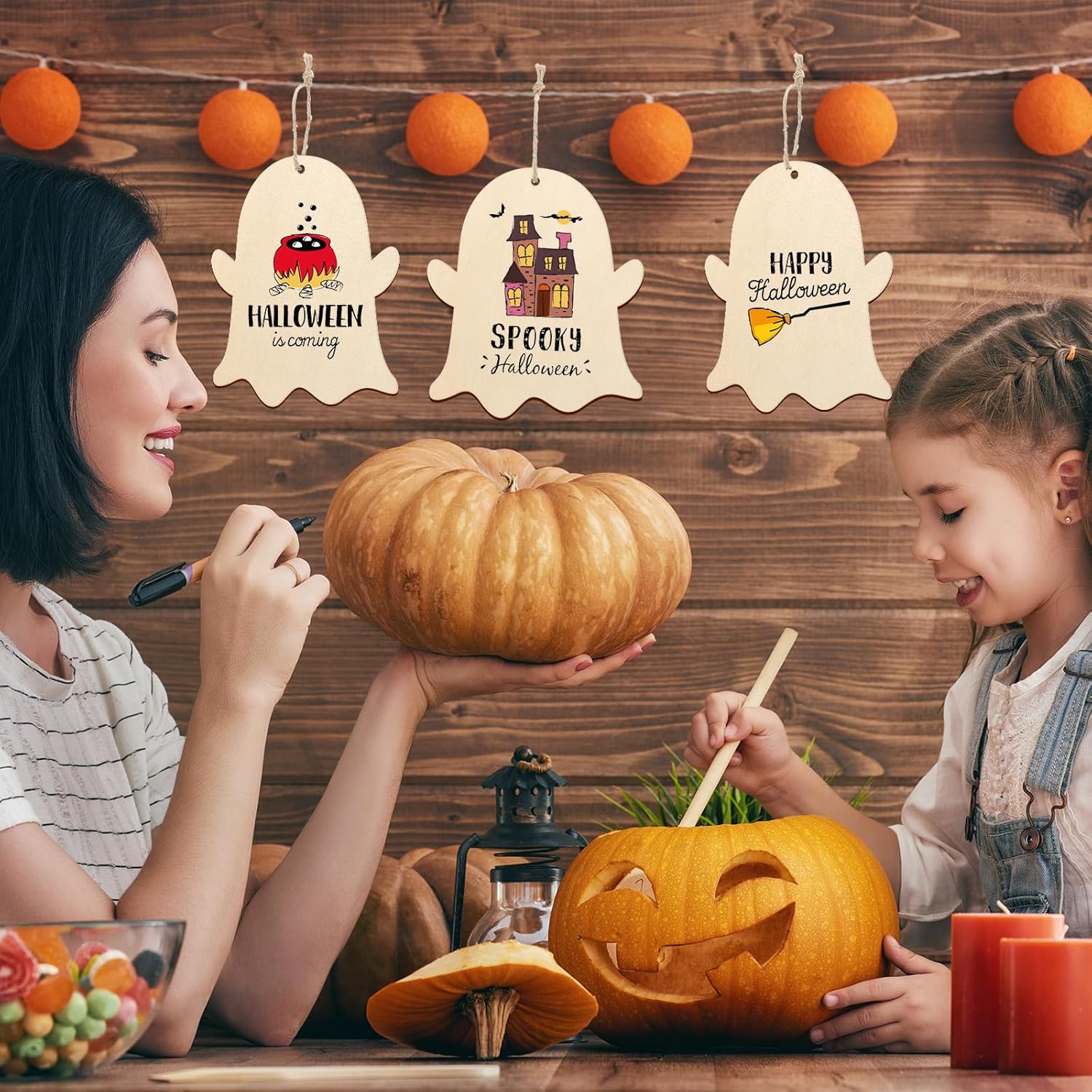 Two women carving pumpkins with Halloween-themed decorations on a wooden wall.
