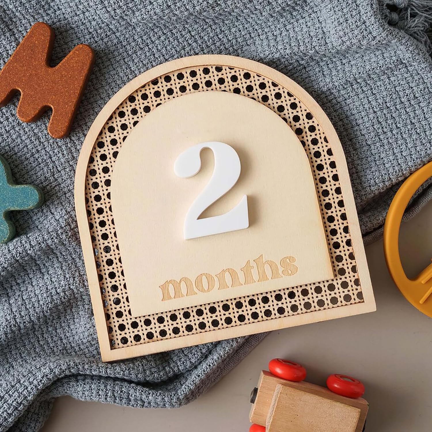Wooden plaque with '2 months' on a textured surface with toys around