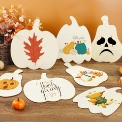 Decorative pumpkin-shaped cards with autumn-themed designs on a wooden surface.