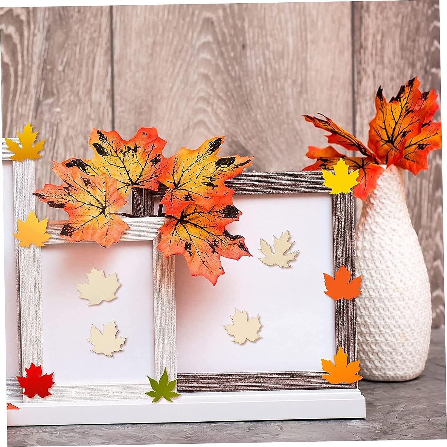 Decorative autumn leaves on a picture frame and vase against a wooden background