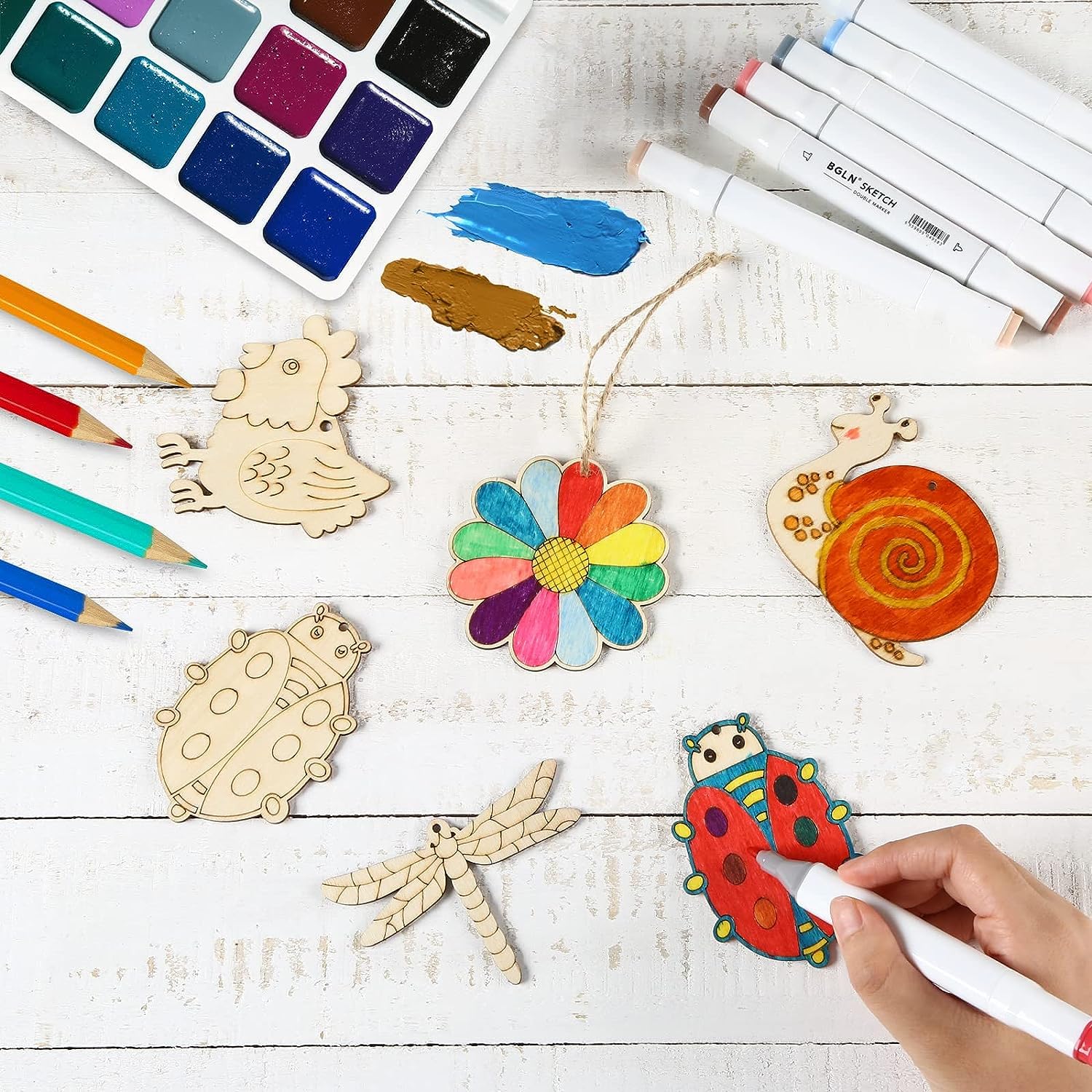 Colorful wooden ornaments on a white surface with art supplies including markers and paint.