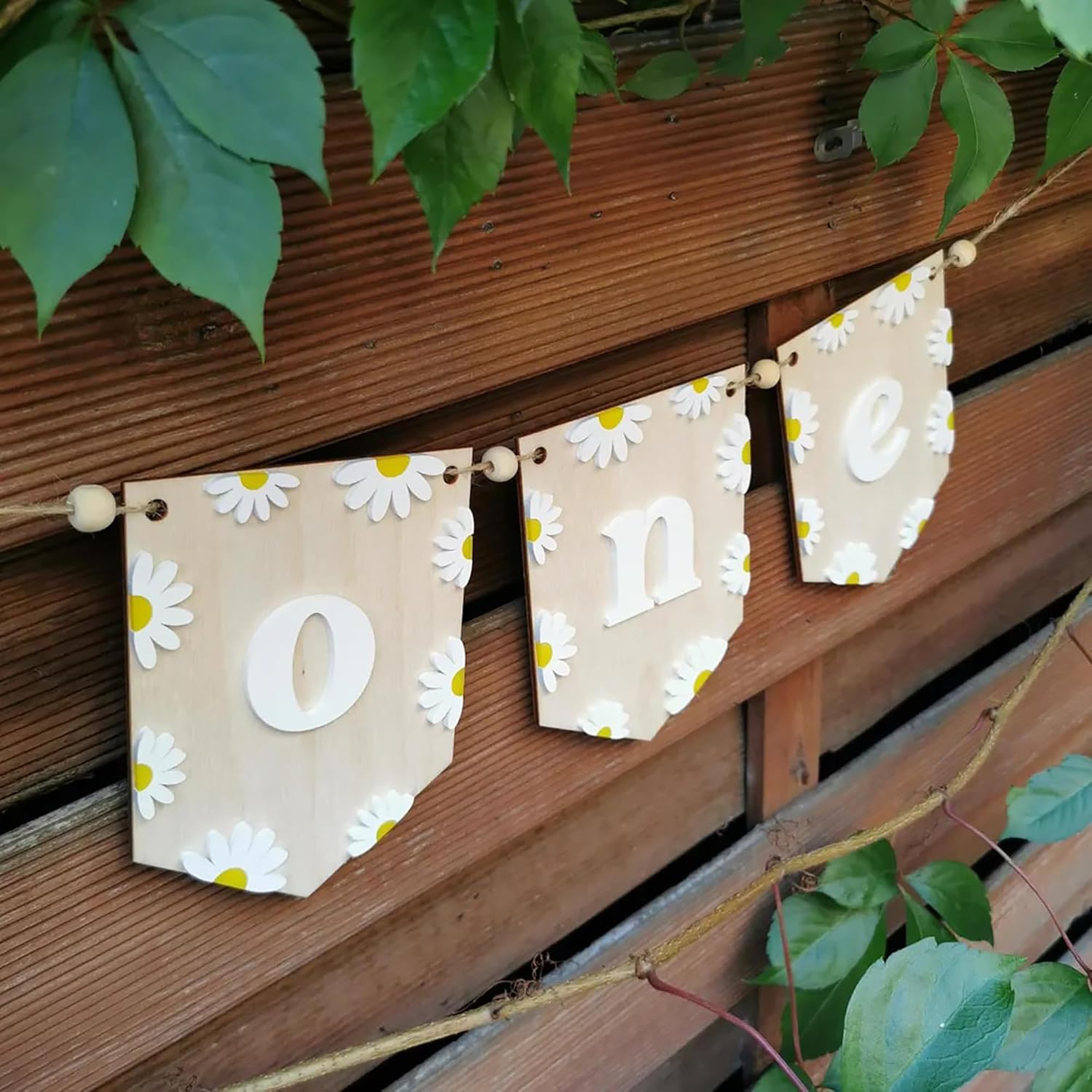 Decorative banner with 'One' and daisy flowers hanging on a wooden wall.