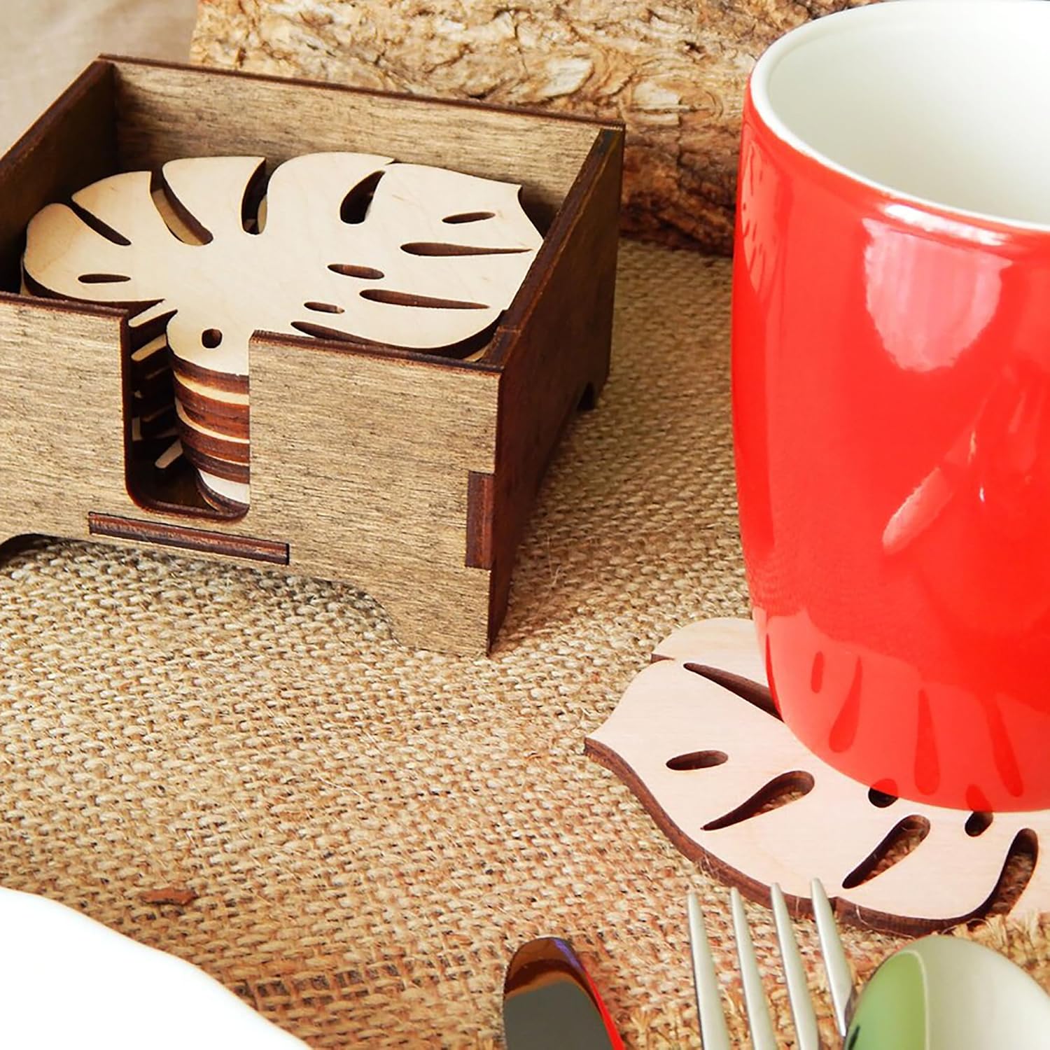 Wooden coaster set with leaf design next to a red mug on a textured surface