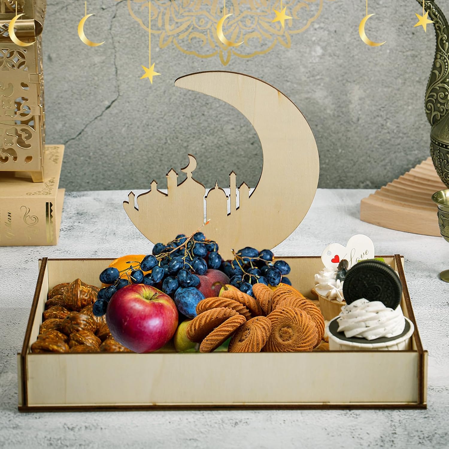 Decorative box with fruits and pastries, featuring a moon and star design, on a textured surface.