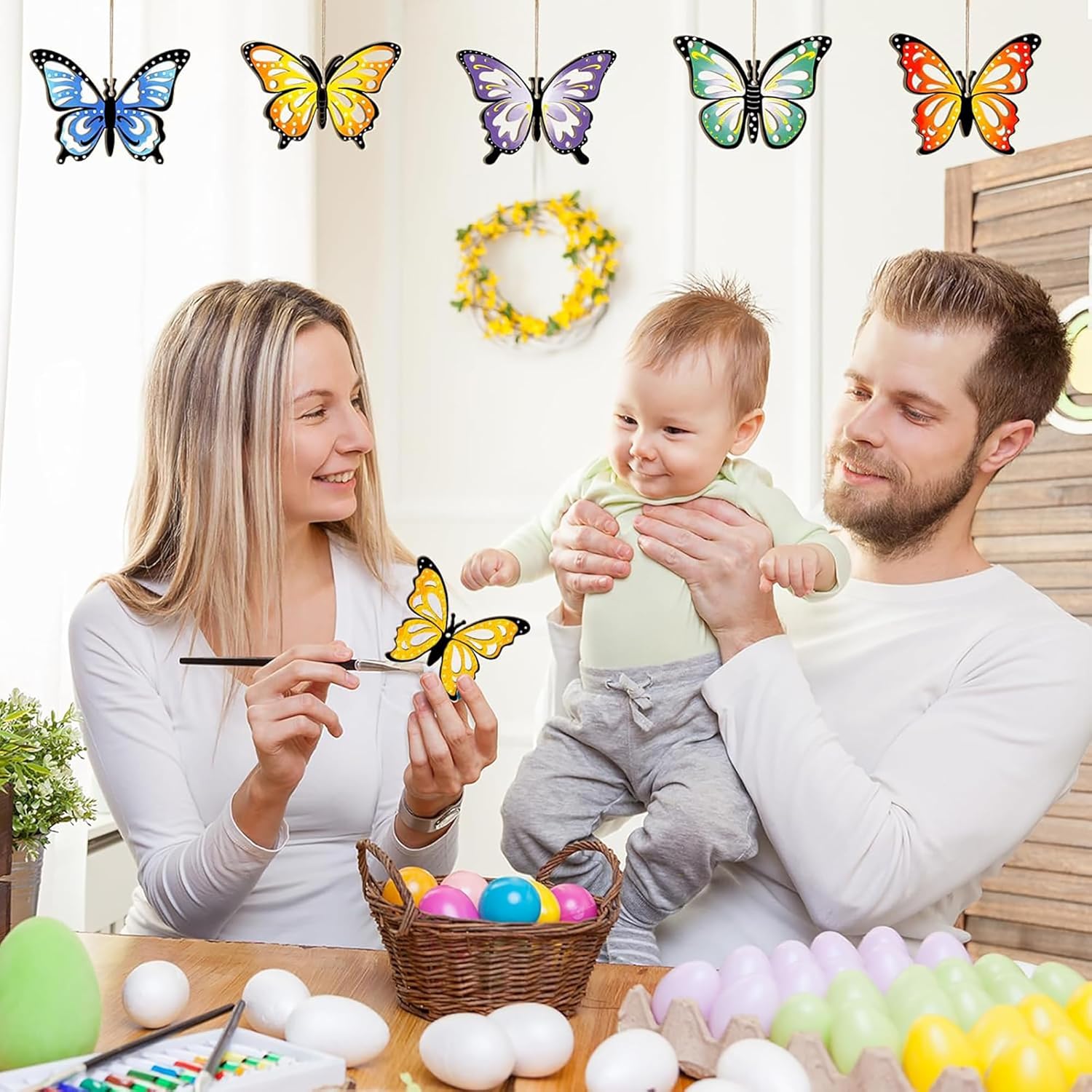 Family with a baby engaging in an Easter egg decorating activity with colorful butterflies displayed above.