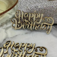 Wooden 'Happy Birthday' decorative piece on a marble surface with a glittery background.