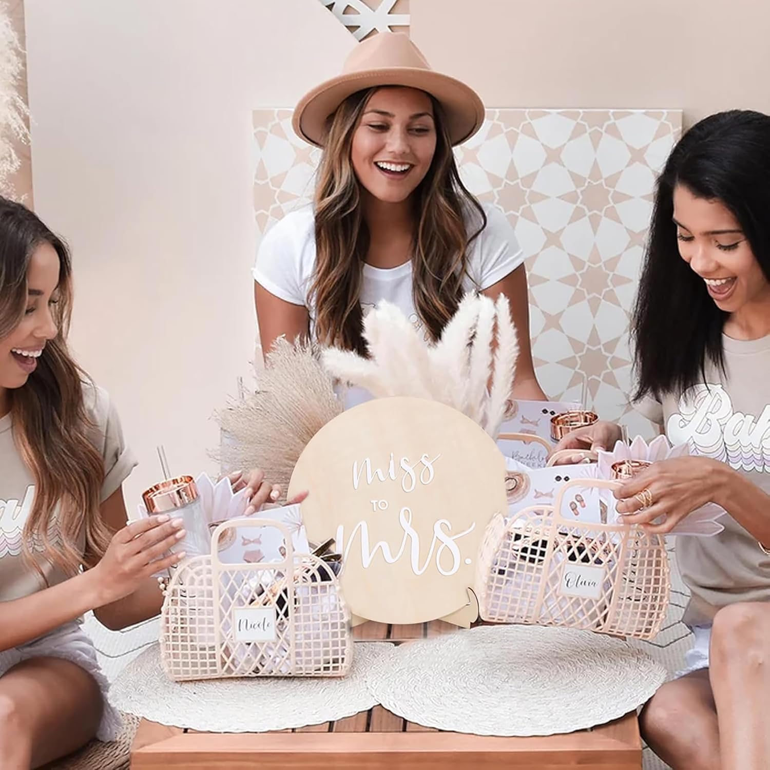 Three women sitting together with a 'Mrs' hat and gift baskets on a table.