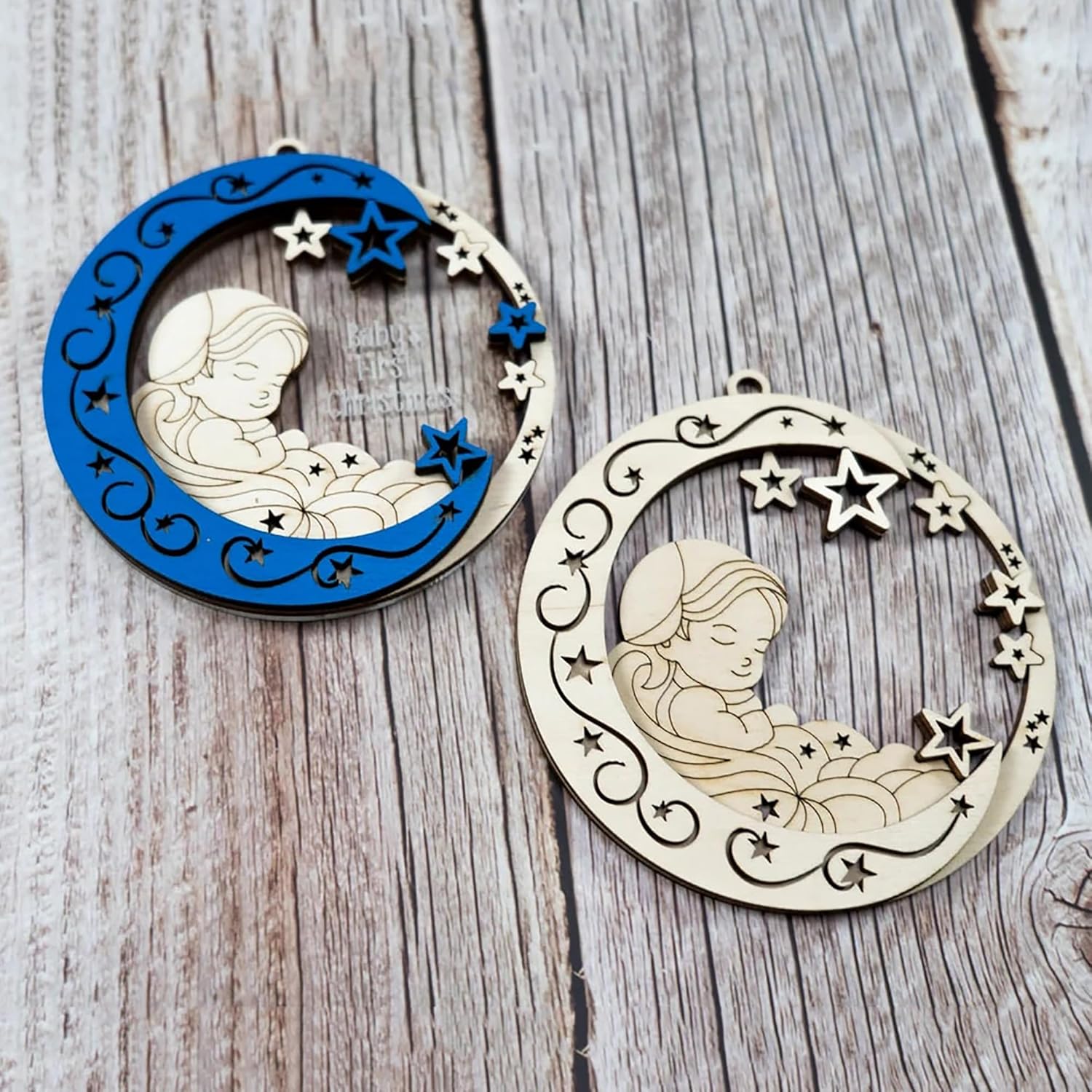 Two decorative ornaments with a design of a child on a crescent moon, one blue and one beige, on a wooden surface.