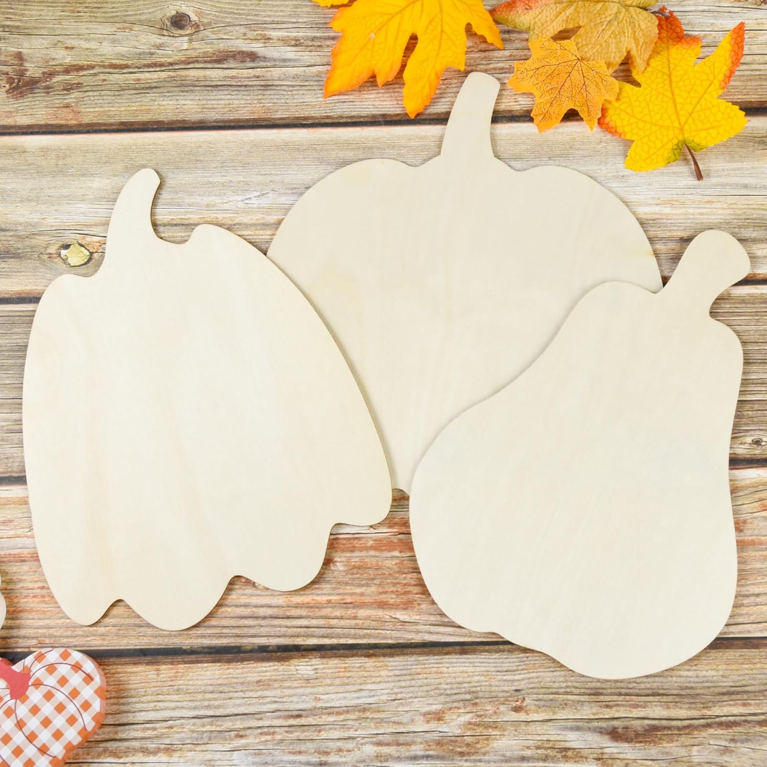 Three wooden pumpkin shapes on a wooden surface with fall leaves.
