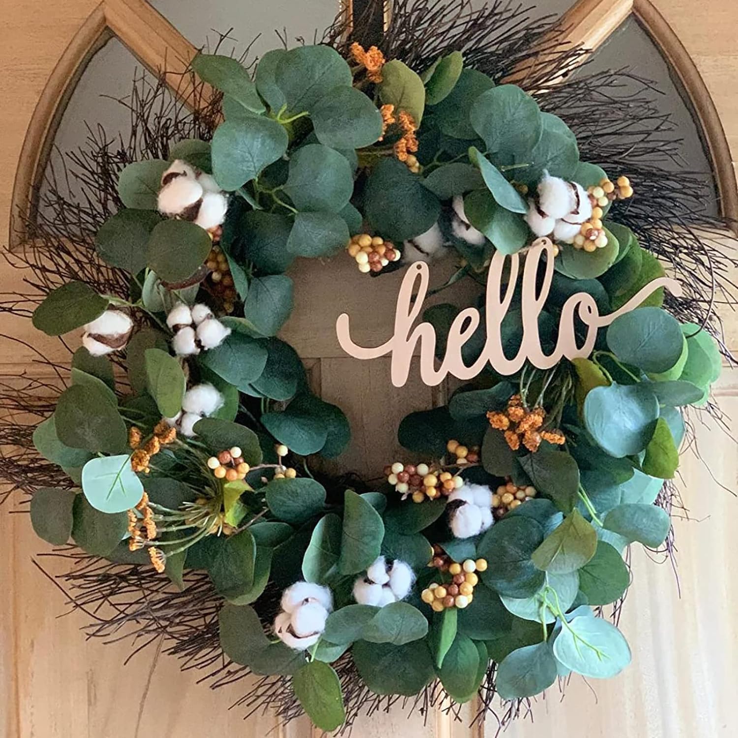 Decorative wreath with green leaves, cotton flowers, and a 'hello' sign on a wooden door.