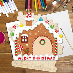 Decorative gingerbread house card with 'Merry Christmas' on a wooden surface with art supplies.