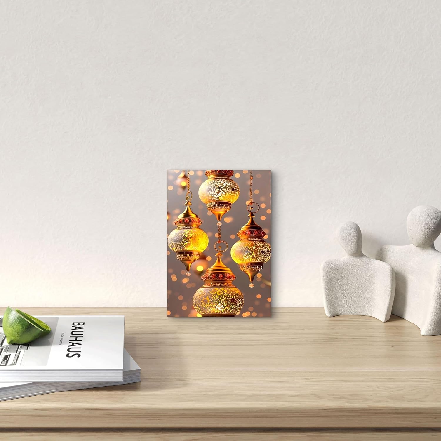 Decorative wall art with gold lanterns on a wooden surface with books and a green apple.
